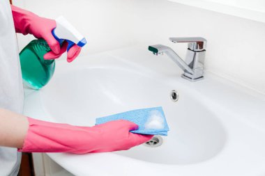 Pembe eldiven giyen kişi beyaz banyo lavabosunu temizlemek için temizlik spreyi ve sünger kullanıyor. Hijyen, temizlik.