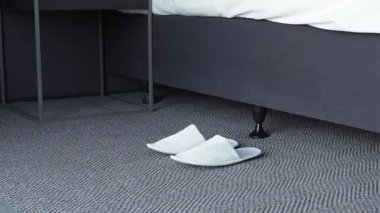 Bir kadın yatağın kenarına yumuşak terliklerini giyer ve sabah rutini çerçeveden çıkar.