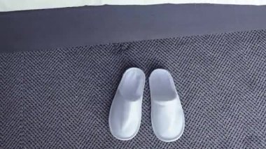 Çıplak ayaklı bir kadın güne başlarken beyaz terliklerin üzerine basar, yukarıdan görünür, sabah rutini.