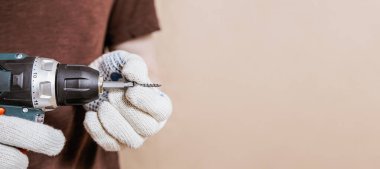 Kişi matkabın kabzasında vida tutacağı yerleştirilirken koruyucu eldivenler giyer, fotokopi alanı olan ev yenileme pankartı takar