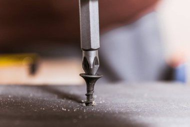 İnşaat sırasında matkap ucu kullanılarak tahtaya tutturulan siyah bir vidanın yakın çekimi.