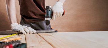Eldivenli bir adam atölyede tahtada elektrikli matkap kullanıyor. DIY, tamir, ev geliştirme