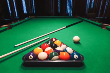 Yeşil bilardo masasında ıstaka çubuklarıyla üçgen bir rafa dizilmiş numaralandırılmış bilardo topları. Bar oyunları, ıstaka sporları