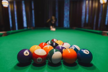 Yeşile basılmış bilardo topları arka planda kırılmaya hazır bir oyuncuyla keçeleşir..