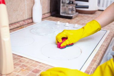Sarı eldivenli eller kir temizler veya beyaz elektrikli ocaktan çıkan yağlar fayanslı mutfak tezgahında sünger kullanırlar, ev temizliği, hijyen...