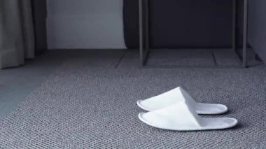 Genç bir kadın yumuşak beyaz terliklerini giyer ve gri halılı bir zeminde çerçeveden dışarı adımını atar ve güne başlar. Sabah rutini, rahat yaşam tarzı