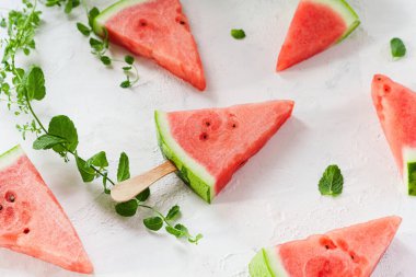 Sopalı bir üçgen karpuz dilimi beyaz arka planda yatıyor. Nane yaprakları ve karpuz dilimleri etrafa saçılmış..