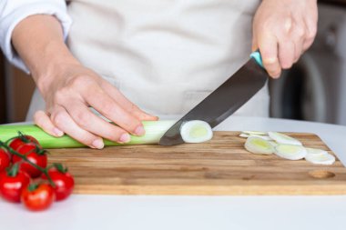 Tahtadaki pırasa halkalarını bıçakla, yemek hazırlama ve sağlıklı pişirme ile kesen ellerin yakın çekimi.