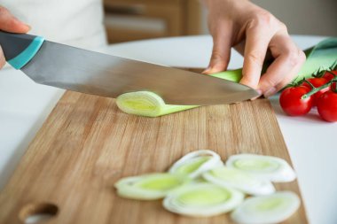 Keskin bıçaklı, yeşil pırasa dilimleyen mutfak masasındaki ahşap tahtada, yemek pişirme rutini, sebze kaplaması.