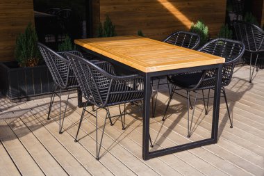 Bahçe veya terasta metal sandalyeli açık ahşap yemek masası, güneş ışığı.