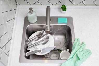 Kirli tabaklar, kaşıklar, bıçaklar ve bardaklar metal bir lavaboda, eldiven ve süngerle birlikte, ev işleri, mutfak temizliği