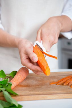 Ahşap kesme tahtasındaki havucu soyarken yakın plan.