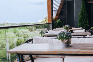 Cafe ahşap masaları, saksı çiçekleri, manzaralı şehir manzarası, yeşillik manzarası, açık hava yemekleri, teras dekoru olan lüks çatı terası.