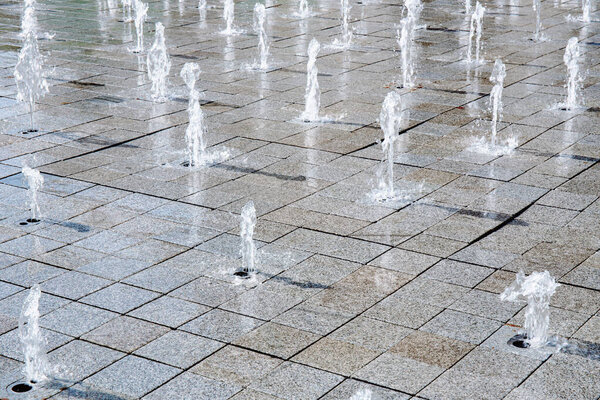 Close-up of urban ground fountains shooting water from tiled pavement in a geometric grid layout, urban landscaping, public spaces