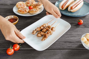 Beyaz bir tabakta servis edilen ızgara yakitori tavuk şişleri, iki elle kırsal bir masada tutulan, çeşitli barlarda atıştırmalıklar.