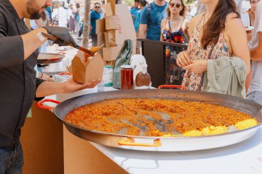 Şef, açık hava şenliği sırasında insanlar sıraya girerken karton bir yemek standında paella servis ediyor. İspanya, Valencia, 05.06.2023.