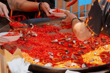 Açık mutfak ekibi deniz ürünleri, ahtapot ve karidesli kırmızı pirinç paella pişiriyor ve servis ediyor.