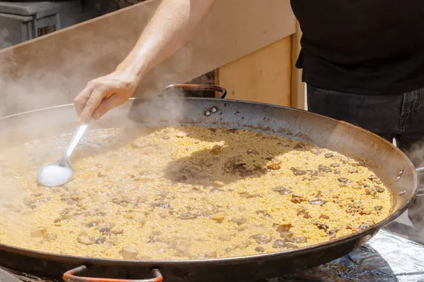 Bir aşçı, halka açık bir yemek festivalinde kaynayan çorbadan yükselen buhar gibi geniş ve sığ bir tavada mantarlı paella karıştırır. İspanyol mutfağı