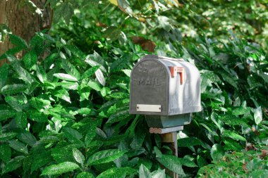 Kırmızı bayraklı klasik posta kutusu yeşilliklerin, açık hava dekorunun ve ev teslimatının arasında duruyor.