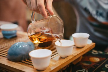 Tören sırasında, saf sürahiden ahşap tepside beyaz fincana altın çay dökülüyor. Zarif çay ritüelinin yakın çekimi..,