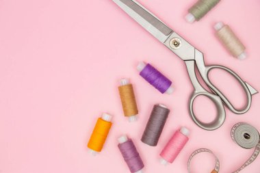 Büyük terzi makasları, parlak iplik makaraları ve yumuşak pembe arka planda bant, dikiş, el işi veya tekstil reklamları, terzilik araçları, tekstil işçiliği için ideal.