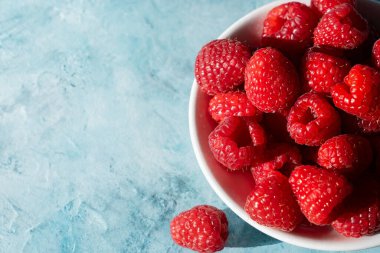 Sulu kırmızı ahududular dokulu mavi yüzeyi doldurur. Bir dut dışarıda dinlenir. Parlak güneş ışığını yakalar.