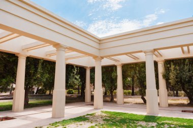 Klasik sütunlara sahip beyaz pavyon İspanya 'nın Valencia kentindeki manzaralı bir parktaki fayanslı zeminin üzerinde temiz gölgeler oluşturuyor.