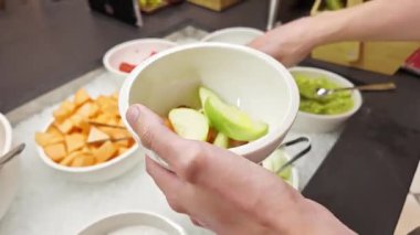 Adam kaseyi dilimlenmiş karpuz ve yeşil elmayla dolduruyor. Kahvaltı büfesinde. Güne sağlıklı bir başlangıç, otel kahvaltısı, sağlıklı beslenme.