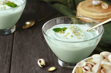 Kremalı şam fıstıklı yoğurt ya da şeffaf cam kasede sunulan ve ahşap arka planda gevrek fındıklı tatlı, süt ürünleri, sağlıklı aromalı tatlı.