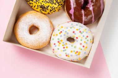 Krema, şeker ve pudra şekerli üç renkli çöreğin yakın plan fotoğrafı. Karton bir kutuda, pastel pembe arka planda, çörek kafe çeşitliliğinde.