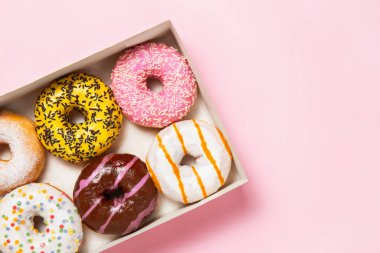 Renkli krema, şerit ve pastel pembe arkaplandaki malzemelerle dolu altı çeşit çörek kutusu.