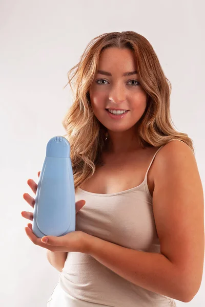 Young woman with bare shoulders holding neutral cream container.