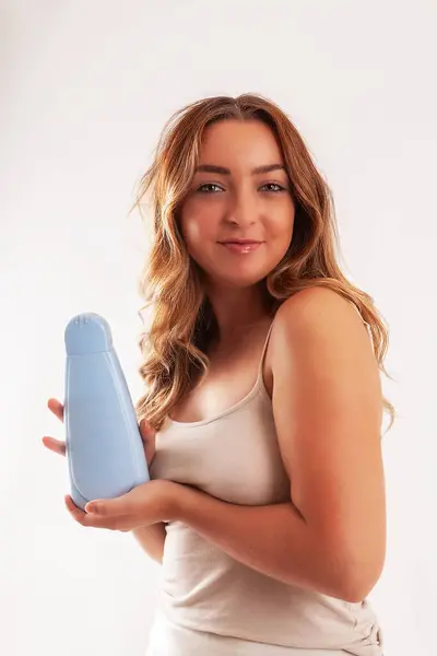 Young woman with bare shoulders holding neutral cream container.
