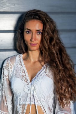 Bu portre, kameraya doğrudan bakan boho tarzı beyaz dantelli bir elbise giymiş genç bir kadını gösteriyor. Uzun, kıvırcık saçları doğal olarak omuzlarına düşüyor ve kıyafetin romantik görünümünü vurguluyor. Elbisenin beyaz danteli, güzel, f
