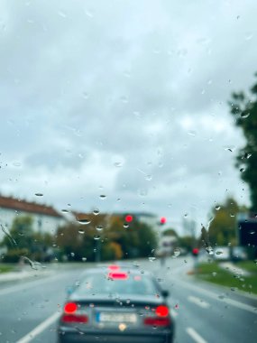 Yağmur, yağmurlu bir günde yolun üzerindeki bir arabanın camına yağmur damlaları yağar. Yoldaki araçlar bir arabanın ön camındaki yağmur damlalarının arkasından görülebilir.