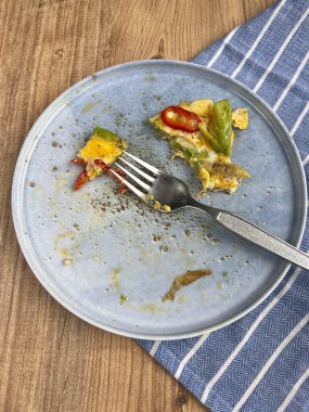 Tahta masadaki tabakta kahvaltı omletinden arta kalanlar. Masada yemek artıklarıyla birlikte mavi tabak. Kahvaltı ya da sağlıklı gıda tüketim konsepti fotoğrafı ahşap zemin üzerinde fotokopi alanı ile