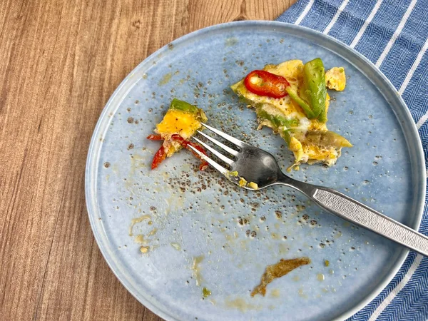 木製のテーブルの上のプレート上の朝食のオムレツの残り物 テーブルの上の青い皿に残り物 コピースペース付きの木の背景にある朝食や健康食品消費のコンセプト写真 — ストック写真