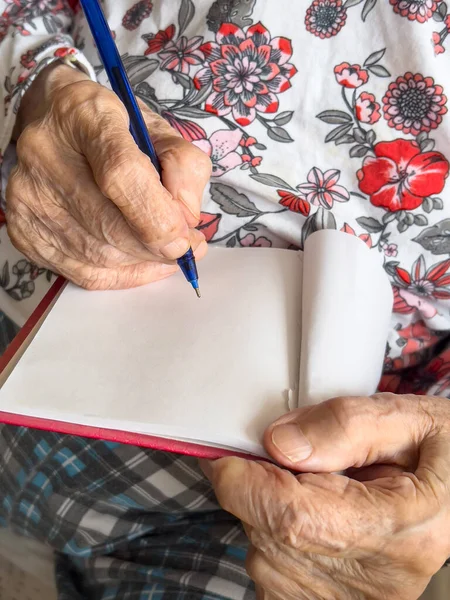 writing, closeup wrinkled hands of old senior woman or person writing note on blank or empty white paper of a notebook. wrinkled hands of old woman with pen and notebook. body part of geriatrics