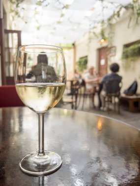 Şarap, masanın üzerinde seçici bir odak noktası olan bir bardak şarap. Gürültü efektleri ve fotokopi alanı olan rahat bir kafe ya da restoranda bulanık insanlar. Masada bir bardak alkol var..