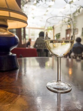 Şarap, masanın üzerinde seçici bir odak noktası olan bir bardak şarap. Gürültü efektleri ve fotokopi alanı olan rahat bir kafe ya da restoranda bulanık insanlar. Masada bir bardak alkol var..