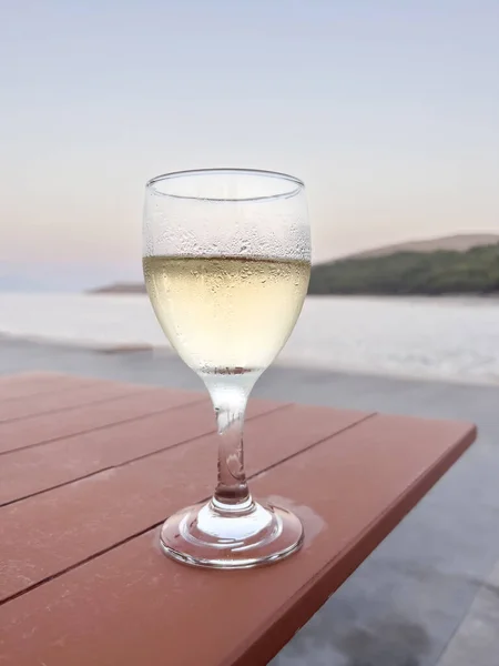 wine, glass of white wine or Prosecco on wooden table over beautiful island and sea view under blue sky with copy space in sunset. glass of cold drink over sea with selective focus