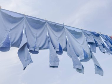 Çamaşırlar, rüzgâr esiyor ıslak giysiler ve mavi gömlekler mavi bahar veya yaz gökyüzü üzerinde fotokopi alanı ile. Ev hanımlarının işi. Açık havada, temiz havada kurutmak için ıslak giysiler ya da temiz gömlekler asmak. Ev işleri.