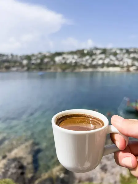 coffee, closeup female hand holds cup of greek or turkish coffee over sea and island under blue sky in a sunny summer day in Turkey. hand holds espresso cup over sea and sky with copy space. hot drink