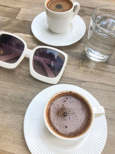 coffee, top view cups of turkish or greek coffee and water glasses on table with beautiful white sunglasses in Turkey or Greece. coffee mugs and water glasses on table. traditional Turkish hot drink