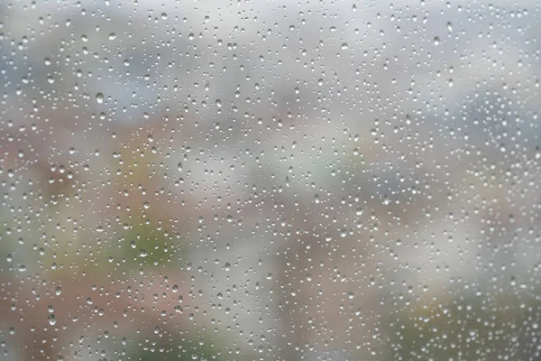 rain, rain drops on windowpane over blurred city view. drops on window against blur background with buildings or houses while raining with selective focus and copy space