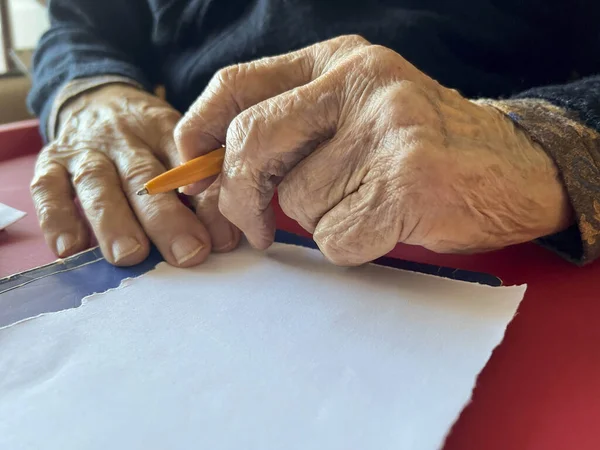 writing, closeup wrinkled hands of old person holding a pen to write on blank or empty white paper. wrinkled body part of senior old woman or man. geriatric people concept photo with body part