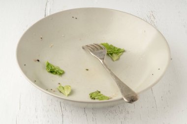 Öğle yemeği için vejetaryen salatasından sonra kirli bir tabakta yemek artıkları ya da masada akşam yemeği. Sağlıklı öğle veya akşam yemeğinden sonra tabakta kalan salata. Sağlıklı gıda konsepti. Kirli bulaşıklar.