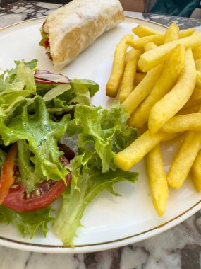 Tabakta ızgara sandviç, öğle yemeğinde salata ve patates kızartması ya da masada akşam yemeği. Fast food konsepti. Salatalı tortilla ve tabakta patates kızartması. Fast food geçmişi