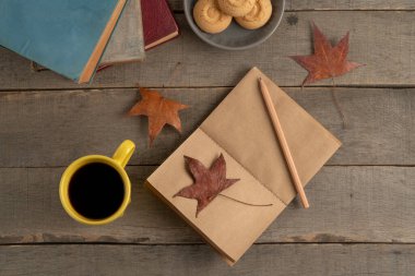 Ahşap masada sonbahar temalı boş bir defter. Kurumuş yapraklar ve boş defterler ahşap arka plan ya da yüzeyde. Masanın üstünde kahve ve kurabiye var. sonbahar konsepti
