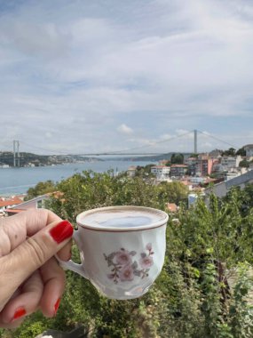 Kahve, yakın plan kadın eli, Türkiye 'nin İstanbul kentindeki güzel bosporus köprüsü ile deniz manzaralı bir fincan Türk kahvesi tutuyor. İstanbul 'da geleneksel Türk kahvesi. Hindi işaretleri. seyahat hedefleri